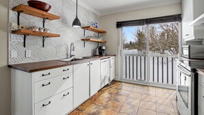 Een keuken met witte kasten, houten planken en een groot raam.