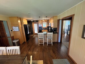 A modern kitchen with wooden cabinets, a black refrigerator, and a dining area with two white chairs. - Cottage on Lake Bellaire July and Aug Openings (Bellaire)