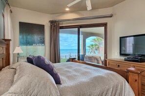 Een hotelkamer met een groot bed, een televisie, uitzicht op het strand en een schuifdeur.