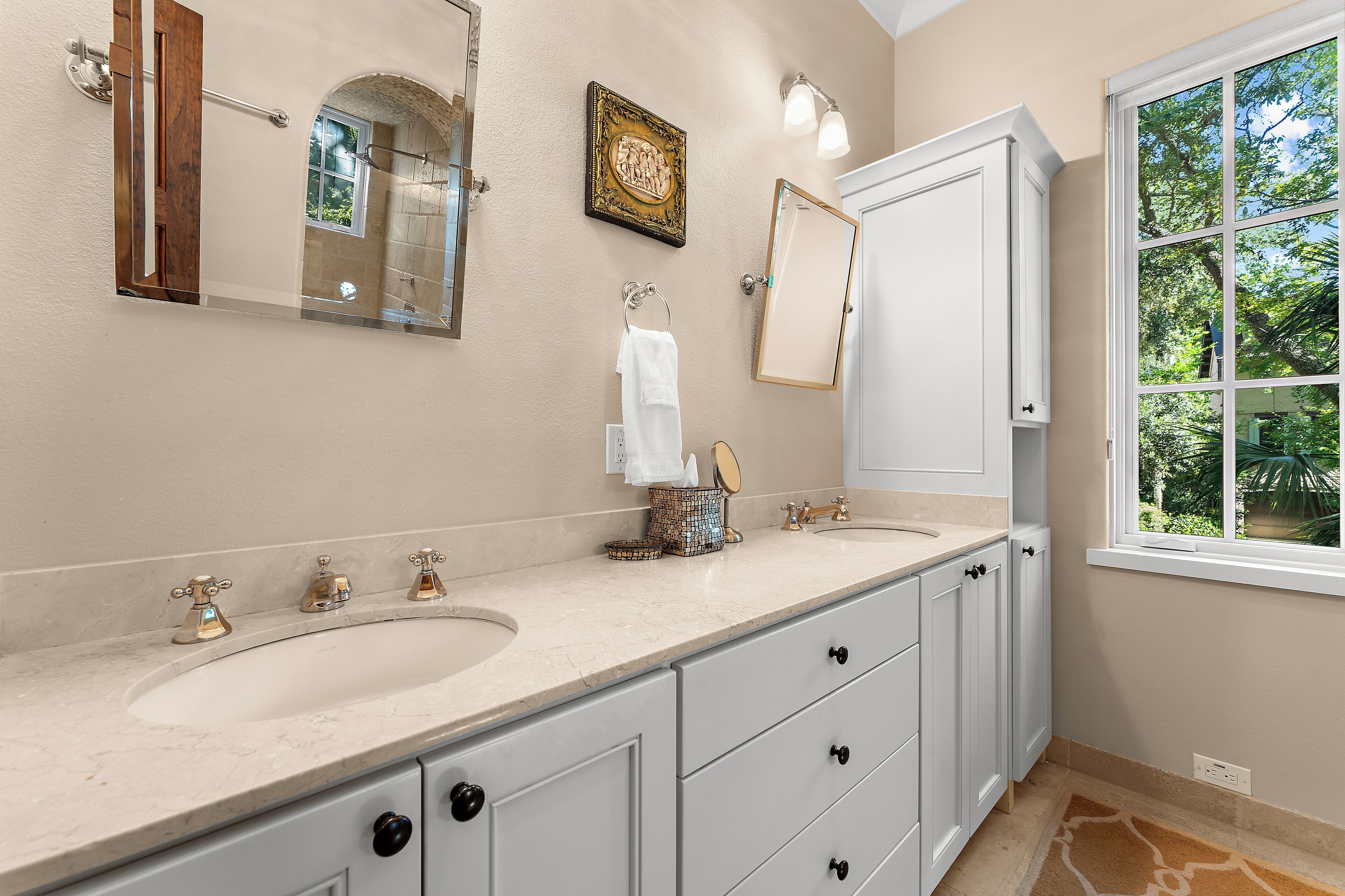 A bathroom with two sinks, a large mirror, and a window with a view of trees.