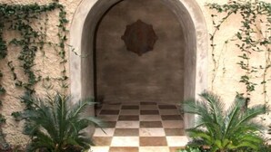 An arched entrance with a lantern, checkered floor, and potted plants.
