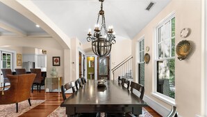 A spacious dining area with a long table, dark wood chairs, and a chandelier.