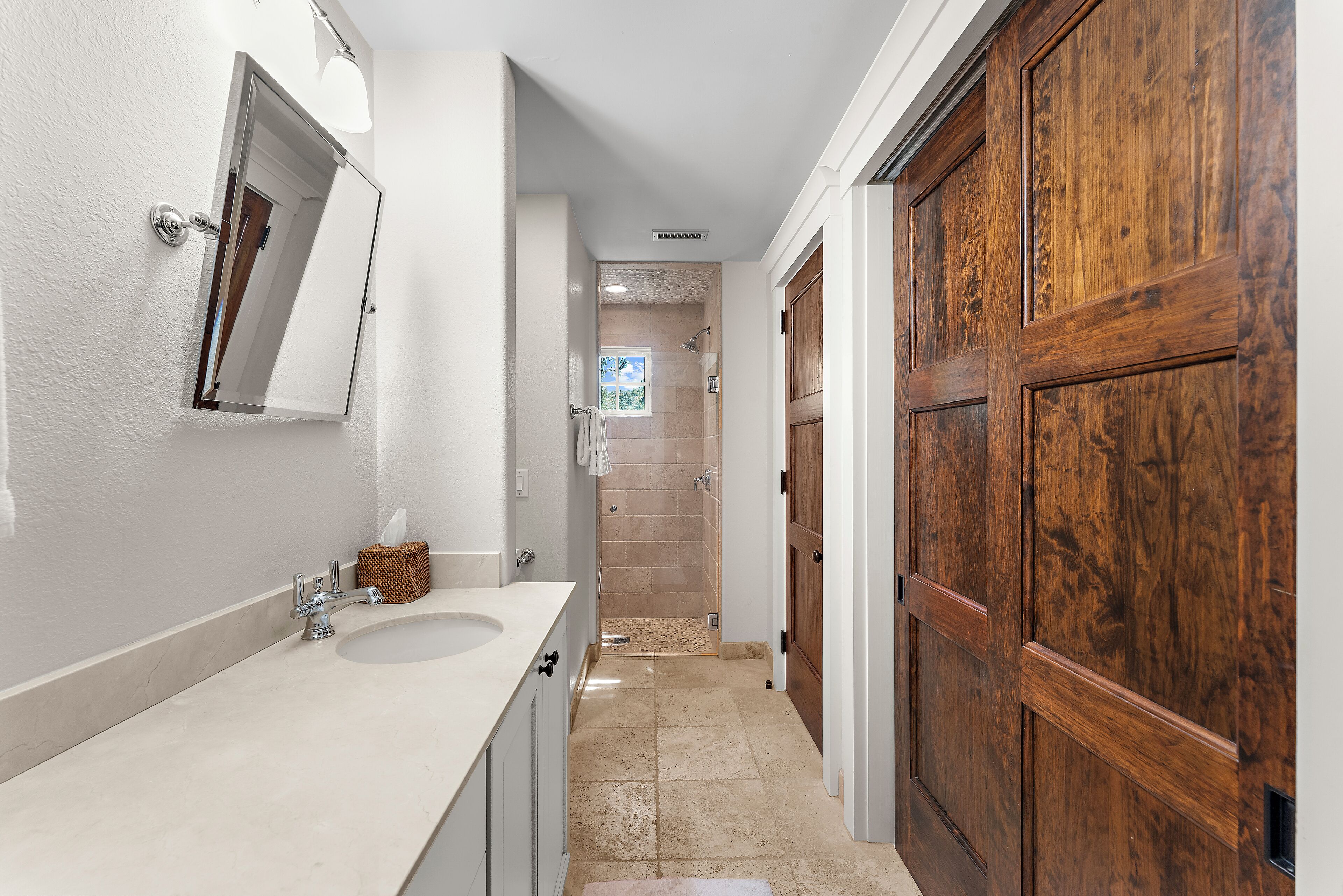 A bathroom with a white sink, a mirror, a wooden door, and a shower area.