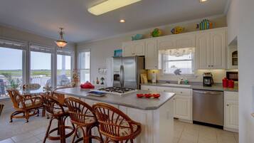 A kitchen with a central island, white cabinets, stainless steel appliances, wicker chairs, and decorative fish on the cabinets.
