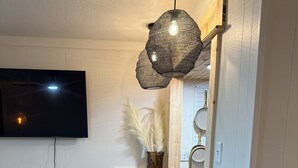 Un comedor con mesa de madera, sillas de mimbre, lámpara colgante y televisor montado en la pared.