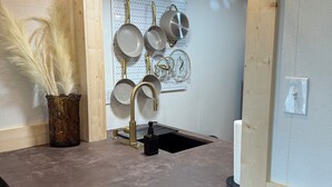 Una cocina con encimera de hormigón, ollas colgantes, un lavabo y dos lámparas colgantes de mimbre.