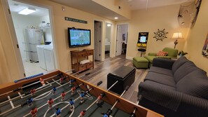 A living room with a foosball table, a television, a Pac-Man game, and a sofa. - MBV 6Br/5Ba - 302B (Myrtle Beach)