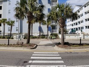 A street view with a crosswalk leading to a building with multiple balconies and palm trees. - MBV 6Br/5Ba - 302B (Myrtle Beach)