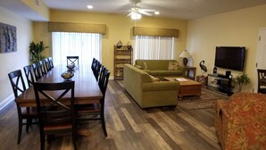 A living room with a sofa, a dining table with chairs, a television, and a ceiling fan. - MBV 6Br/5Ba - 302B (Myrtle Beach)
