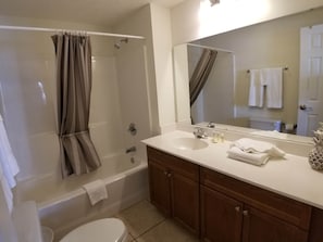 A bathroom with a shower, toilet, sink, and mirror.