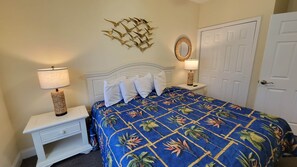 A bedroom with a bed, two bedside tables, a wall-mounted mirror, and a door.
