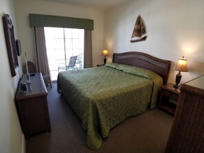 A hotel room with a large bed, two bedside tables with lamps, a chair, a desk with a lamp, and a window with curtains.