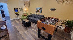 A living room with a foosball table, a green armchair, a sofa, a lamp, and a wall clock. - MBV 6Br/5Ba - 302B (Myrtle Beach)