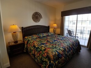A hotel room with a large bed, two bedside lamps, a decorative wall piece, and a balcony with a chair.