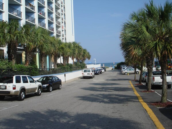 A street lined with parked cars, palm trees, and a tall building with balconies. - MBV 6Br/5Ba - 302B (Myrtle Beach)