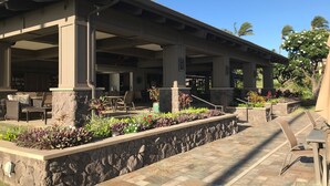 Un patio extérieur couvert, doté de murs en pierre et d’un sol carrelé, comprenant un espace salon extérieur et un jardin aménagé.