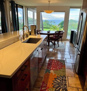 A kitchen with a large island, a dining area with a view, and a refrigerator.