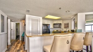 A kitchen with white cabinets, a black refrigerator, a microwave, and a stove. There are three beige bar stools. - Gorgeous direct oceanfront- end unit in highly desirable location! 
 (North Myrtle Beach)