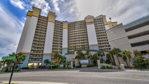 A multi-story hotel with a central entrance, palm trees, and a clear sky. - Gorgeous direct oceanfront- end unit in highly desirable location! 
 (North Myrtle Beach)