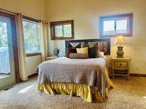 A bedroom with a bed, a nightstand, a lamp, and two windows.