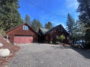 A two-story wooden house with a red garage, surrounded by trees and a gravel driveway.