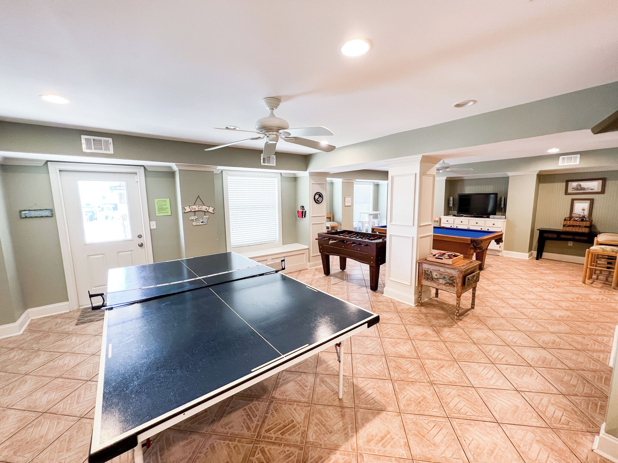 A spacious room with a ping pong table, a foosball table, and a pool table.