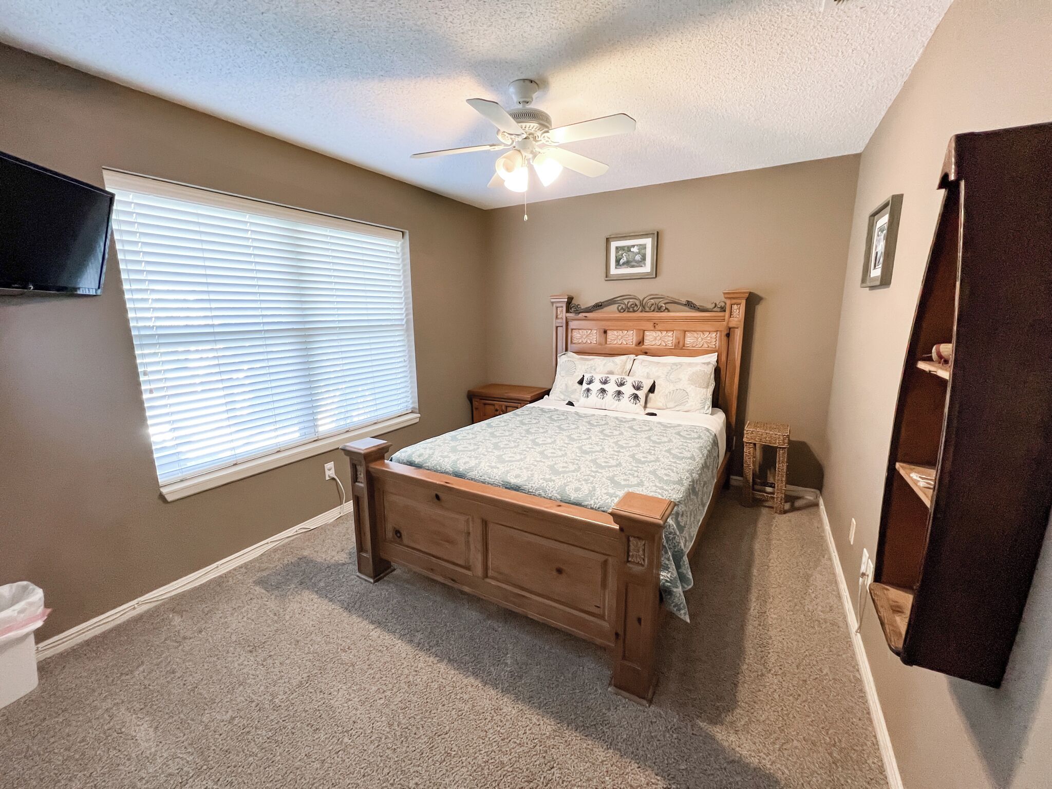Une chambre à coucher avec un lit en bois, un ventilateur de plafond, une fenêtre avec des stores, une table de chevet et une armoire.