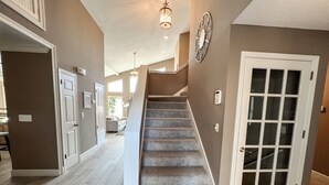 Un couloir avec un escalier recouvert de moquette, une porte dotée d’un panneau en verre et un luminaire fixé au mur.