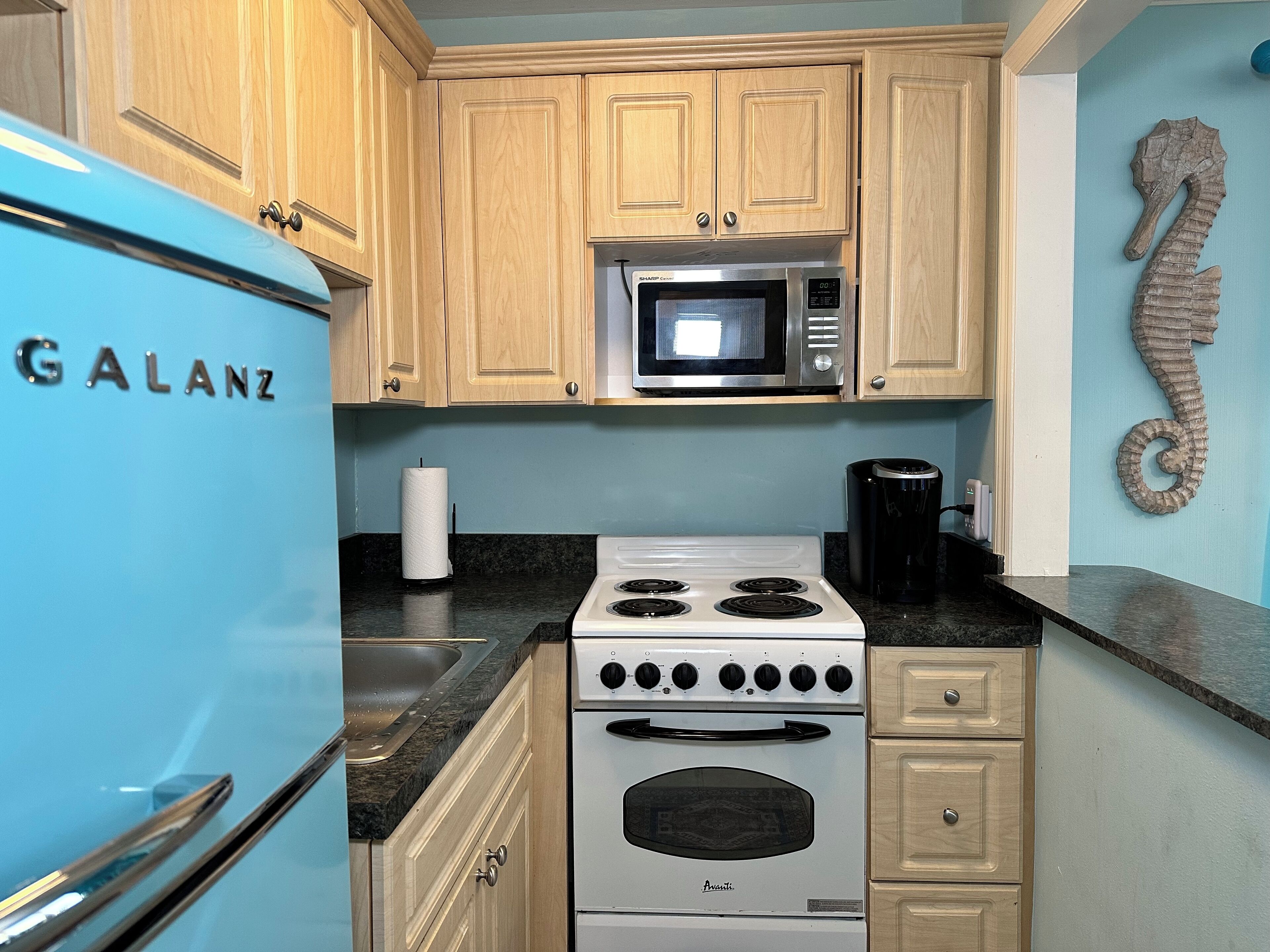 A kitchen with wooden cabinets, a microwave, a stove, and a Galanz refrigerator.