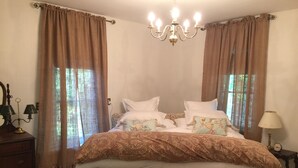 A bedroom with a large bed, a wooden chest, a nightstand with a lamp, and a chandelier. - Renovated 1854 Sea Captain's House w/Harbor Views in Deer Isle Village (Deer isle)