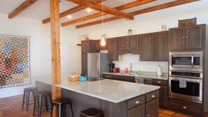 Une cuisine avec des poutres en bois, des meubles de couleur sombre, un îlot central avec des tabourets et des appareils électroménagers modernes.