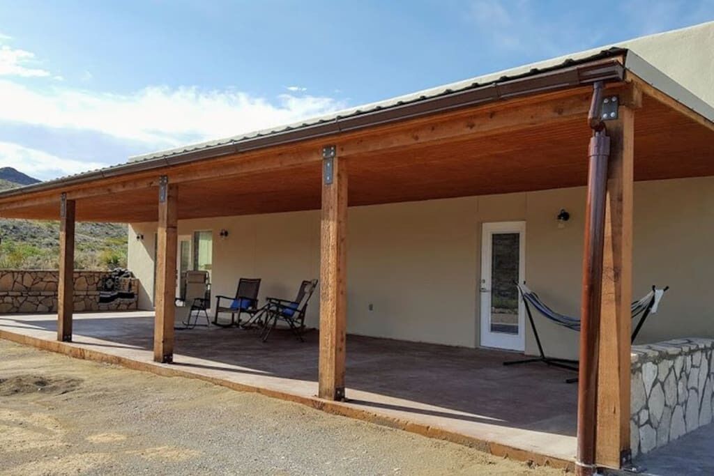 Un espace extérieur abrité, doté d’un mur en pierre, de piliers en bois et d’une porte.