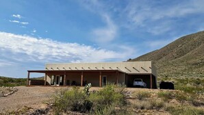 Un bâtiment moderne doté d’un patio couvert, d’un garage et offrant, en arrière-plan, un paysage désertique.