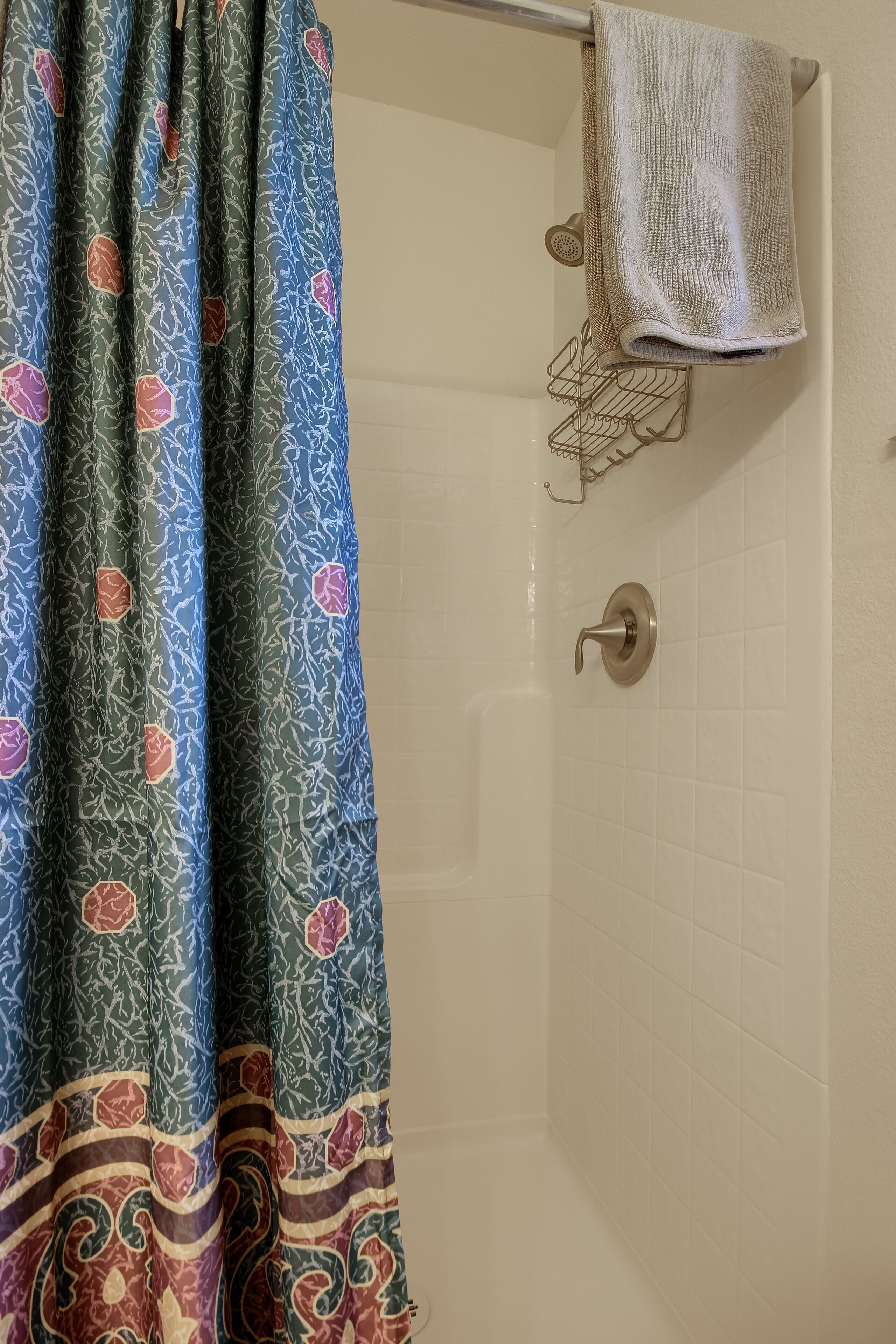 A bathroom with a shower curtain featuring a floral pattern, a towel rack with a white towel, and a shower door with a metallic handle.