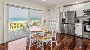 A kitchen with a view of the ocean, white cabinets, stainless steel appliances, and a wooden dining table with chairs. - Beach's Edge, On the beach (Captiva)