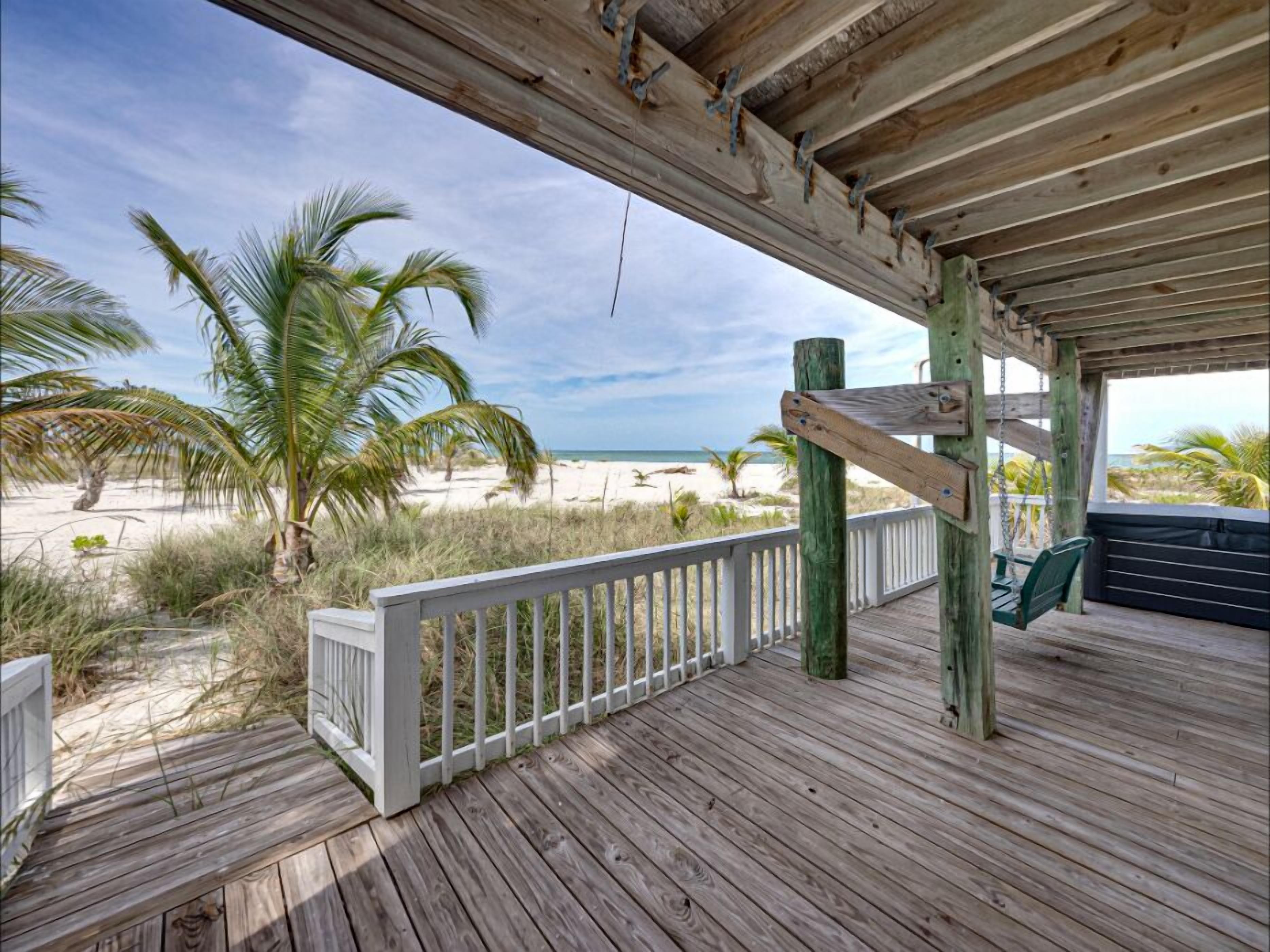 A wooden deck with a white railing overlooking a beach with palm trees and the ocean.