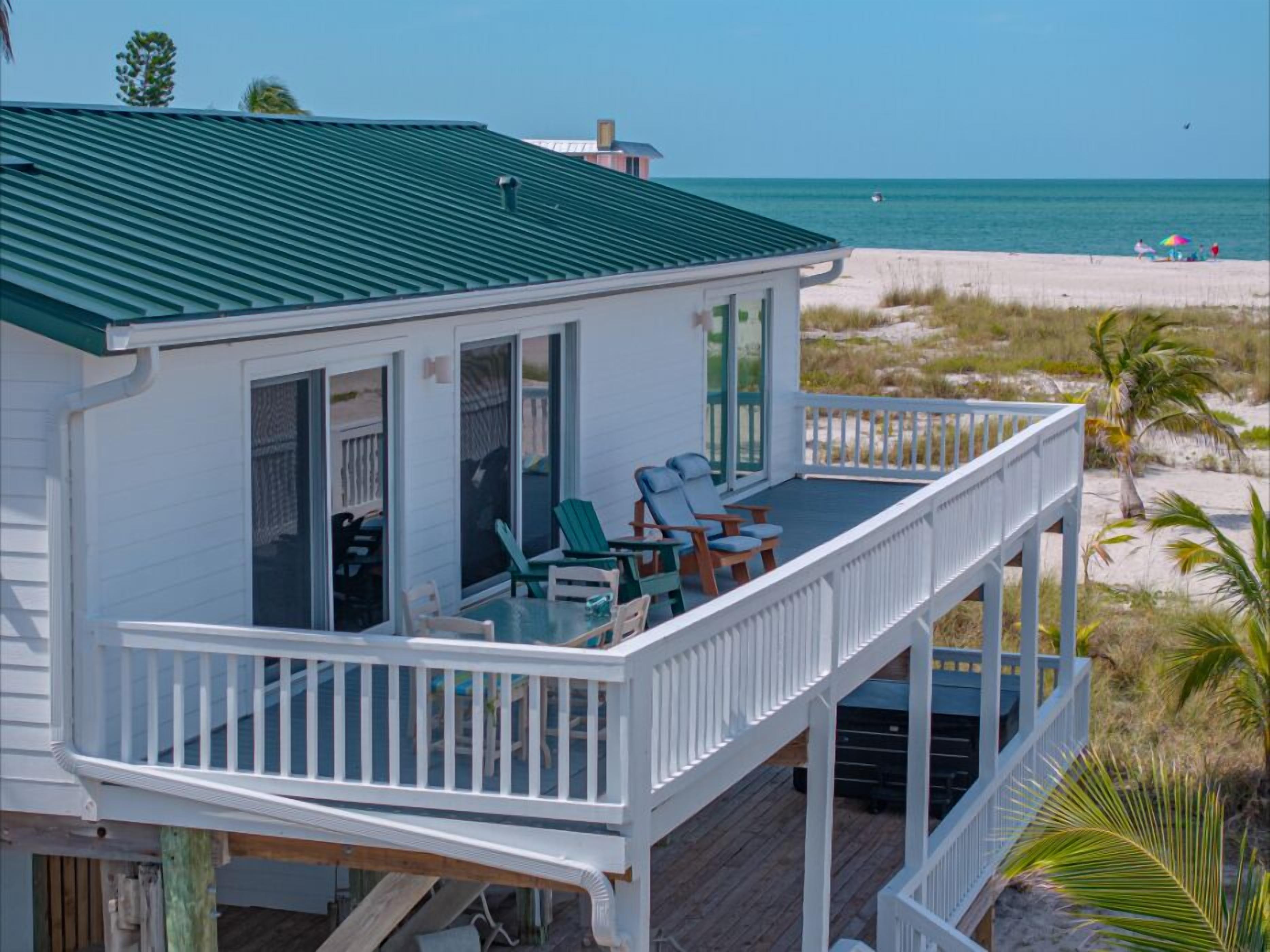A beachfront house with a covered porch, outdoor seating, and a view of the beach.