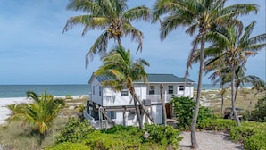 A beachfront house with a balcony, surrounded by palm trees and vegetation. - Beach's Edge, On the beach (Captiva)