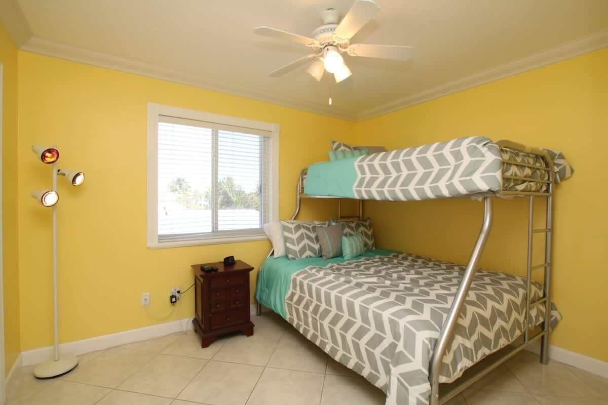 A room with a bunk bed, a standing lamp, a window, and a ceiling fan.