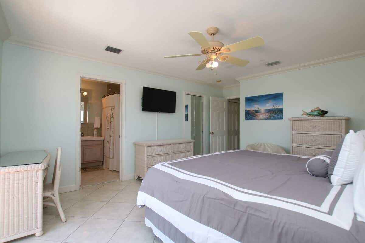 A bedroom with a bed, a ceiling fan, a television, a dresser, and a painting on the wall.