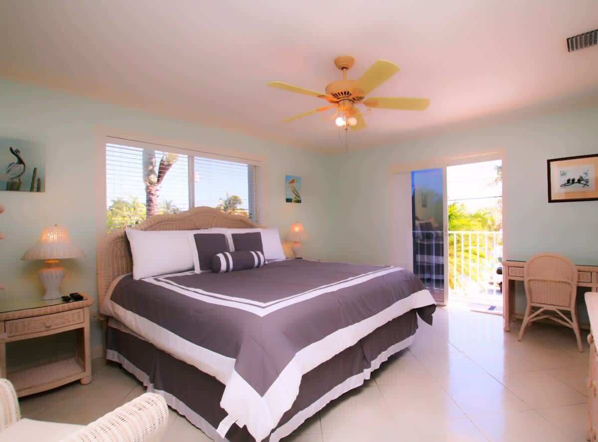 Une chambre à coucher avec un lit, des tables de chevet, un ventilateur de plafond et une vue sur l’extérieur.