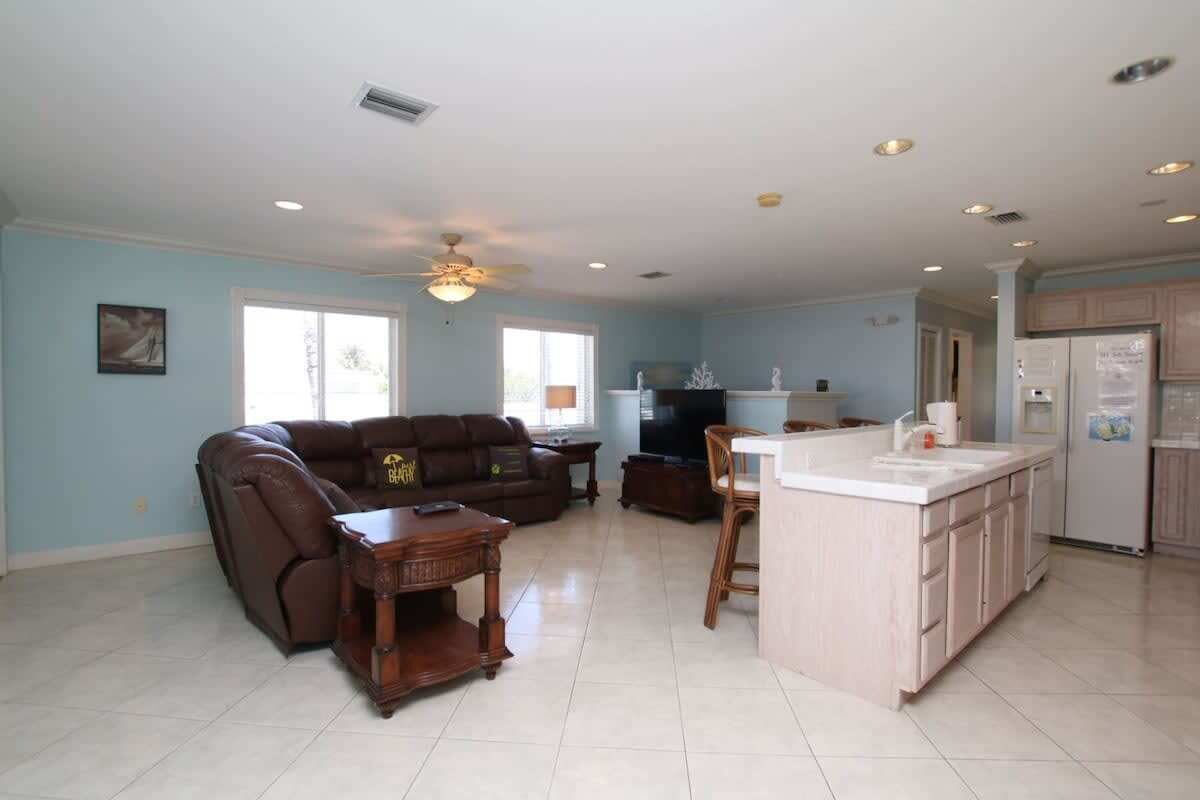 A spacious living area with a brown leather sofa, a wooden coffee table, and a kitchen island with a sink.