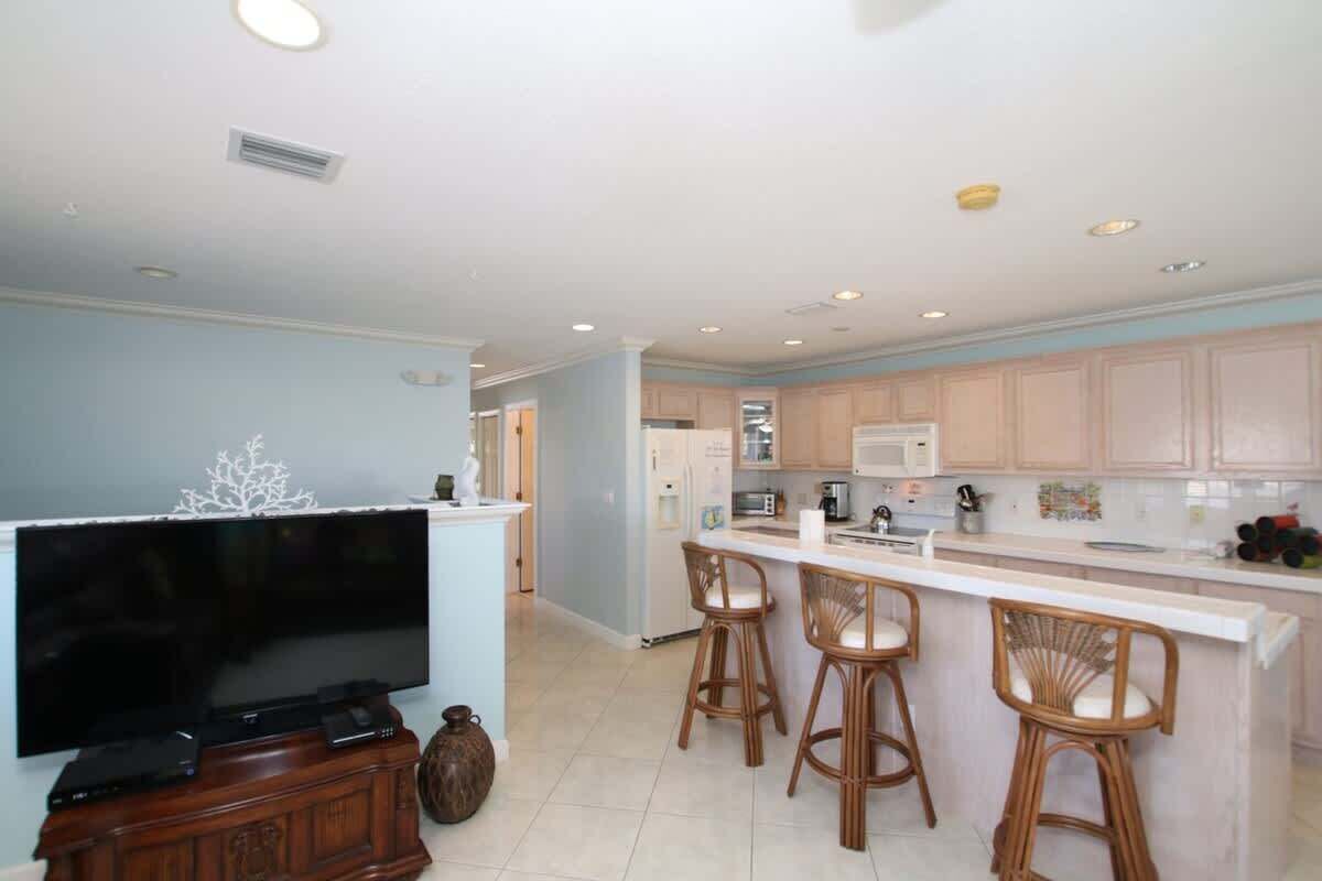 A modern kitchen with a central island, bar stools, and a flat-screen TV.