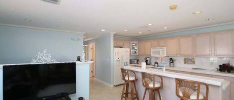 A modern kitchen with a central island, bar stools, and a flat-screen TV.