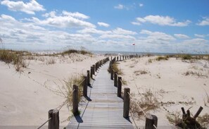 A wooden boardwalk leading to the beach, surrounded by sand dunes and sparse vegetation.