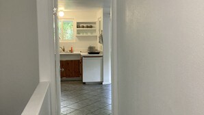 A narrow hallway leading to a kitchen with white walls, a tiled floor, and wooden cabinets. - 1 Mile from Pipeline Surf Break! (Haleiwa)