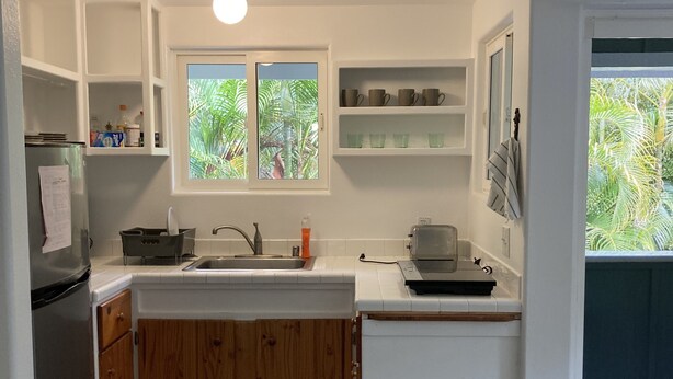 A kitchen with white cabinets, a wooden countertop, a sink, a refrigerator, and a window with a view of greenery. - 1 Mile from Pipeline Surf Break! (Haleiwa)