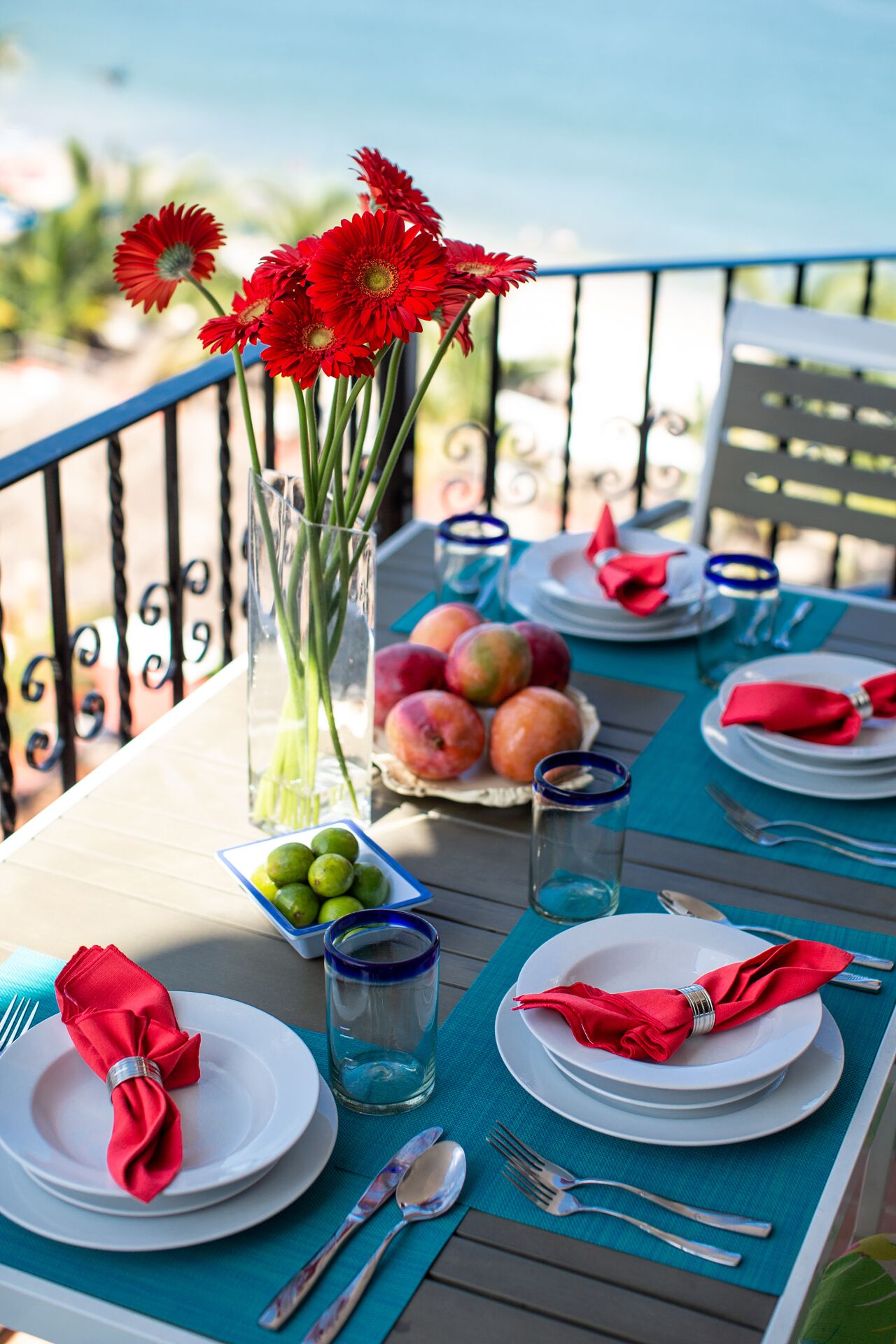 Une table mise pour un repas, avec des assiettes, des couverts et un vase rempli de fleurs rouges.