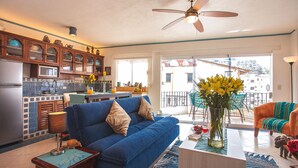 A living room with a blue sofa, a coffee table, and a kitchen area with wooden cabinets and a refrigerator.