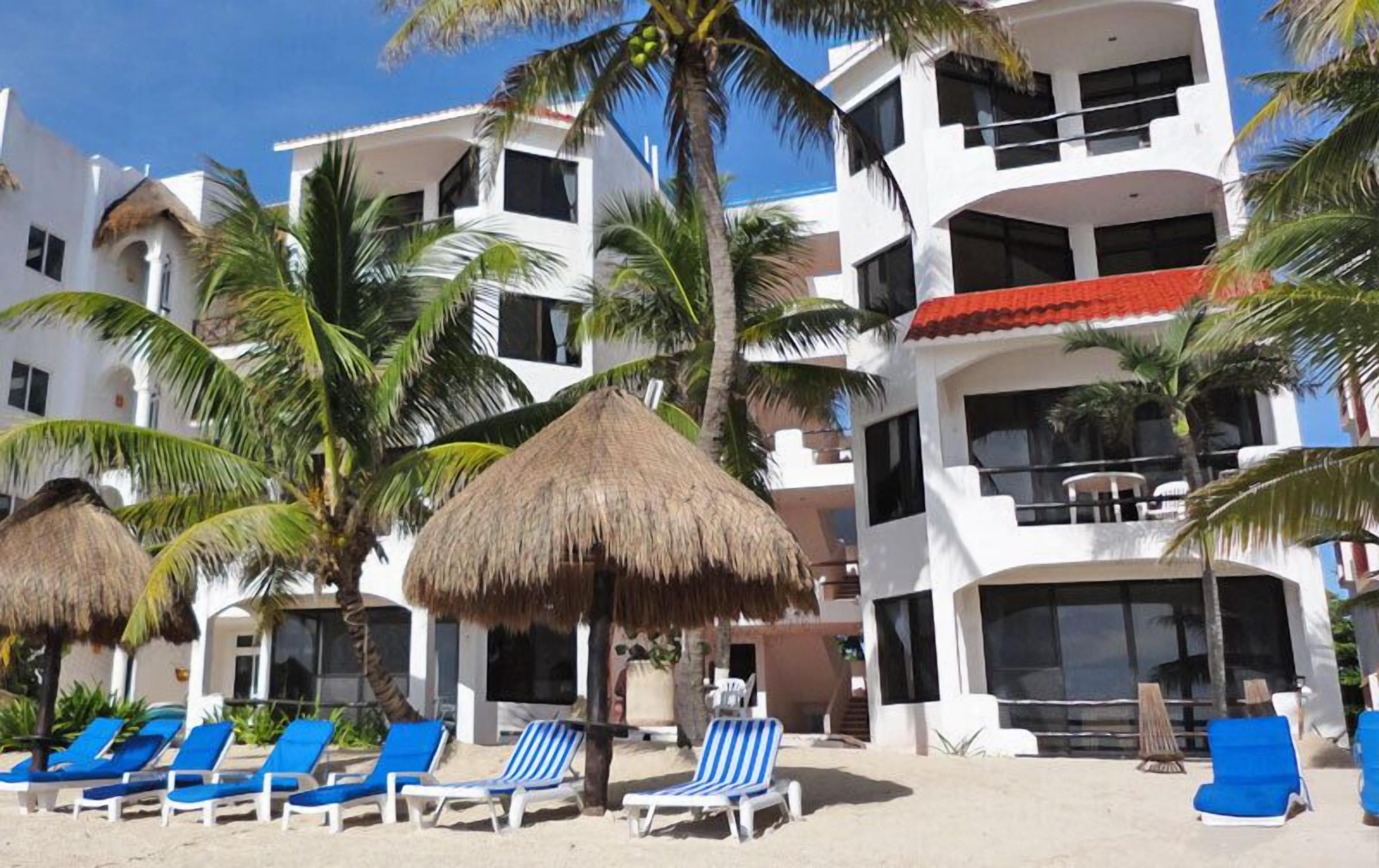 A beachfront hotel with multiple balconies, palm trees, and sun loungers.